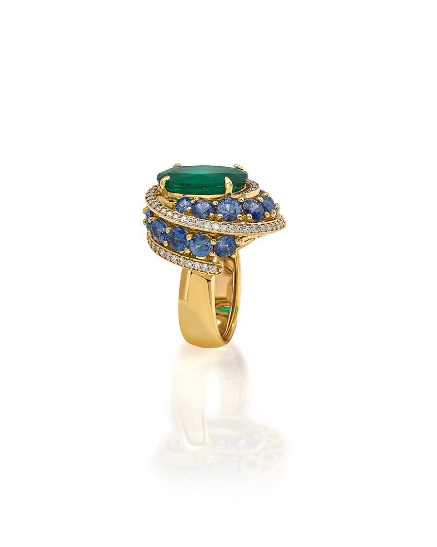 Ring in 18kt yellow gold set with white diamonds (0.66 cts), blue sapphires (4.86 cts), and one oval shape emerald center stone (7.46 cts)